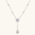 Sterling silver necklace with cushion-cut moissanite in halo setting and teardrop pendant, displayed on cream background.