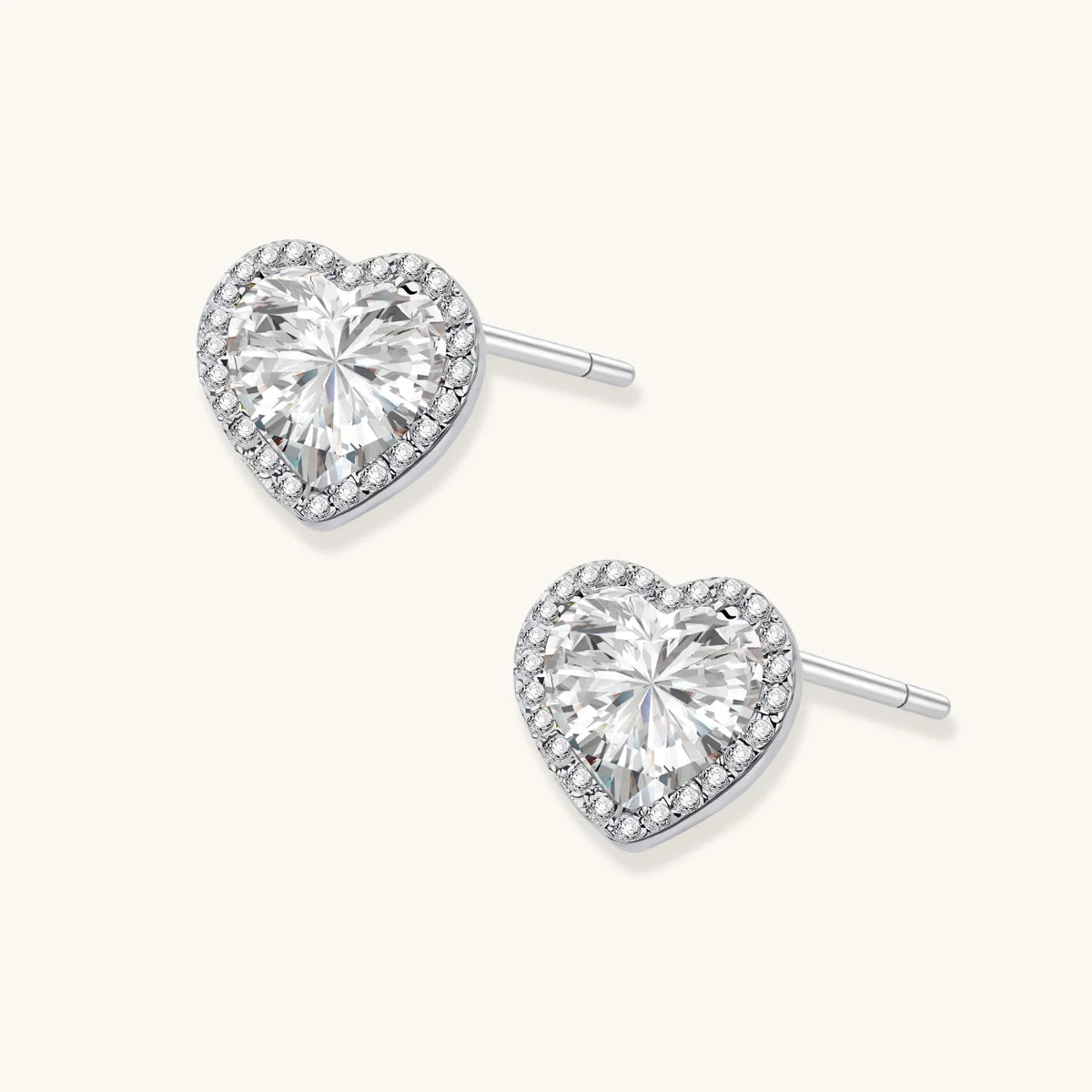 Close-up of heart-shaped moissanite stud earrings in sterling silver halo setting on cream background.