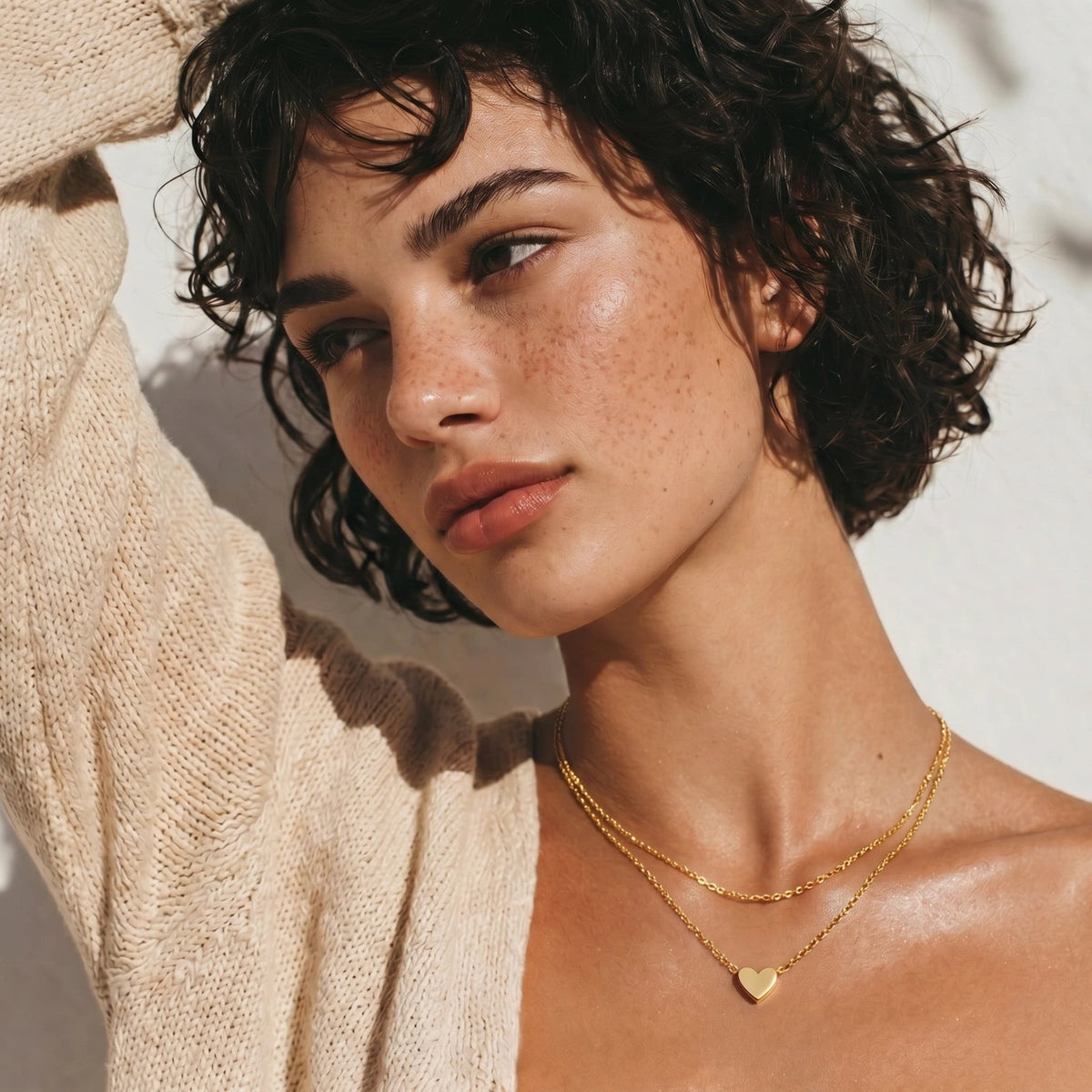 Havora layered gold heart necklace on a woman with short dark hair wearing a beige knitted cardigan